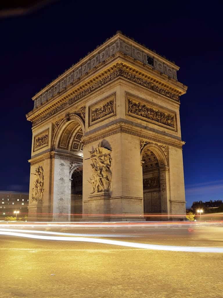 Elegant night shot of the Arc de Triomphe in Paris with light trails underneath, capturing its monumental beauty.