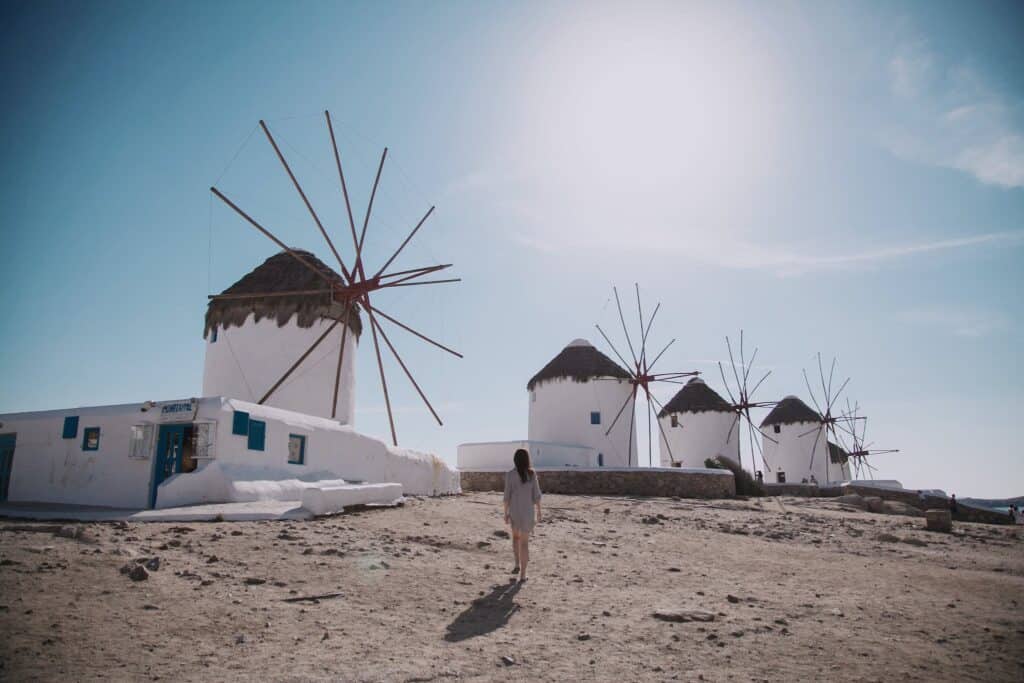 Woman Wearing Grey Dress Walking In Front Of Windmill Under Blue Sky